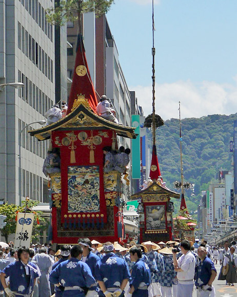 写真：青い法被姿の人達が山鉾を引いて街中を練り歩いている様子